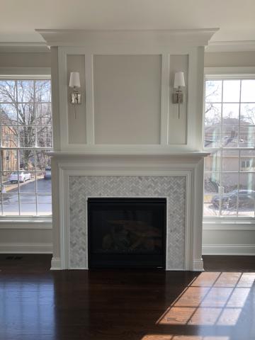 Fireplace with marble herringbone tiles and   wall sconces